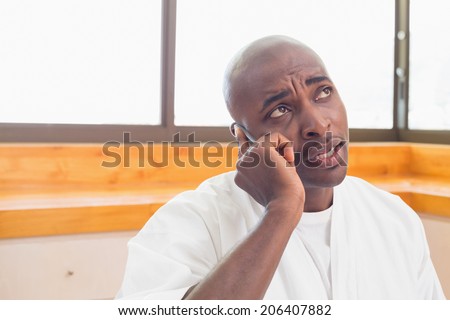 Serious man in bathrobe talking on phone at home in the kitchen