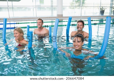 Happy fitness class doing aqua aerobics with foam rollers in swimming pool at the leisure centre