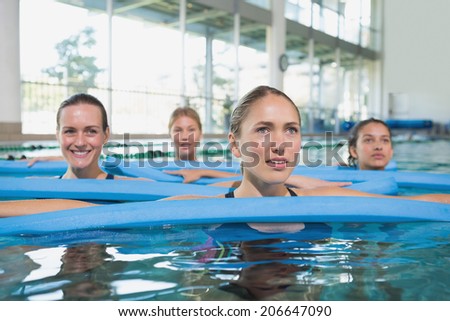 Female fitness class doing aqua aerobics with foam rollers in swimming pool at the leisure centre