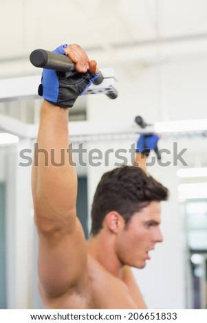 Side view of a shirtless male body builder doing pull ups at the gym