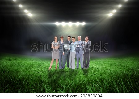 Business team looking at camera against football pitch with bright lights