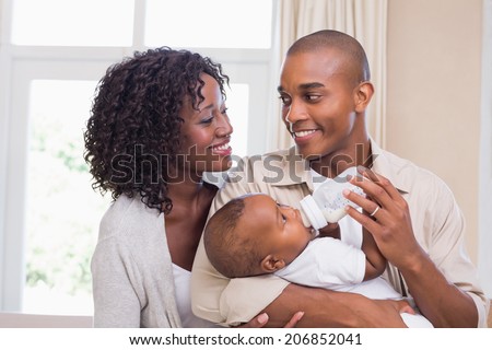Happy parents feeding their baby boy a bottle at home in the bedroom