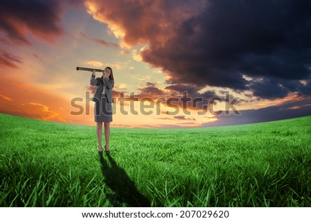 Businesswoman looking through a telescope against green field under orange sky