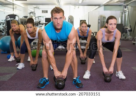 Muscular instructor leading kettlebell class at the gym