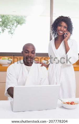Happy couple in bathrobes in the kitchen using technology at home in the kitchen