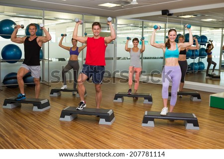 Fitness class doing step aerobics with dumbbells at the gym