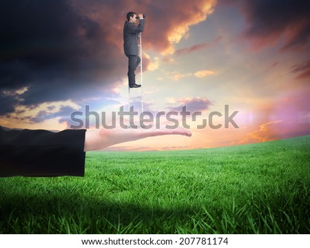 Businessman standing on ladder against green field under orange sky