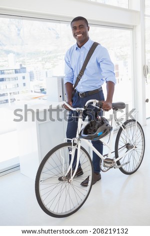 Happy businessman standing with his bike in his office