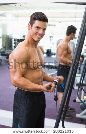 Side view portrait of a shirtless young muscular man using triceps pull down in gym