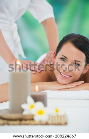 Beautiful brunette enjoying a back massage smiling at camera at a luxury spa