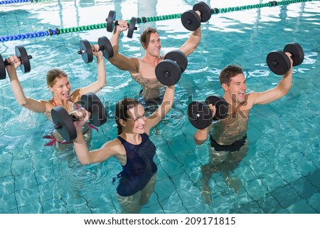 Happy fitness class doing aqua aerobics with foam dumbbells in swimming pool at the leisure centre
