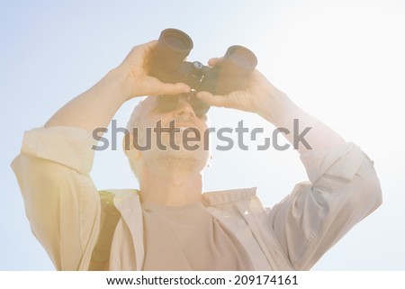 Happy hiker looking through binoculars on a sunny day