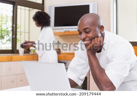 Handsome man in bathrobe using laptop at table at home in the kitchen