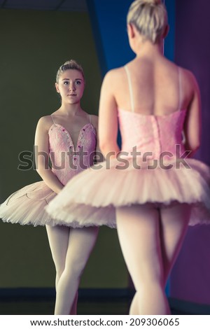 Graceful ballerina standing in first position in front of mirror in the ballet studio
