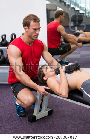 Personal trainer helping client lift dumbbells at the gym