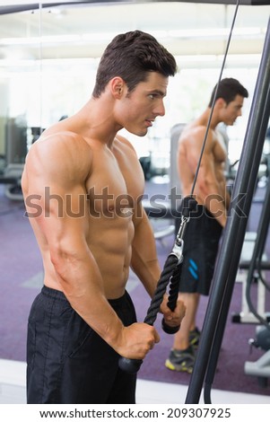 Side view of a shirtless young muscular man using triceps pull down in gym