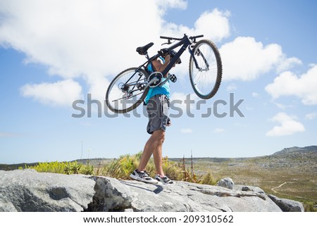 Fit man walking on rocky terrain holding mountain bike on a sunny day