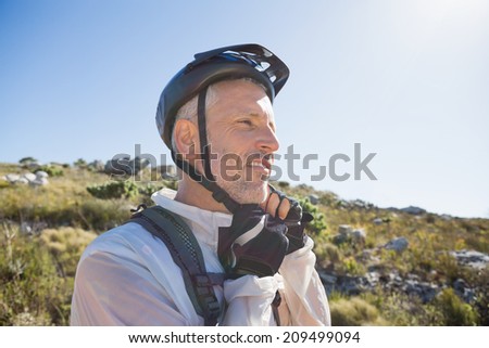 Fit cyclist adjusting helmet strap on country terrain on a sunny day