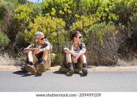 Hitch hiking couple sitting on the side of the road on a sunny day