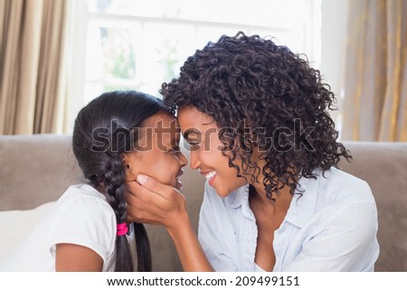 Pretty mother sitting on couch with cute daughter at home in the living room