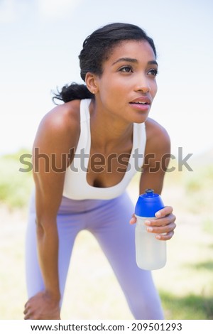 Fit woman holding sports bottle smiling on a sunny day in the countryside