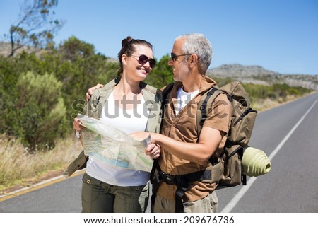 Hiking couple looking at map on the road on a sunny day