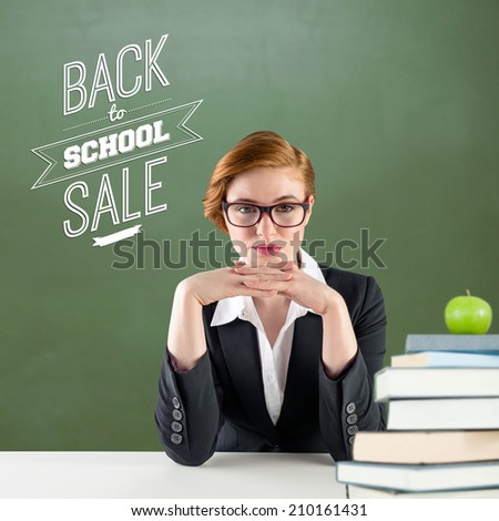 Redhead teacher sitting at desk against green apple on pile of books in classroom