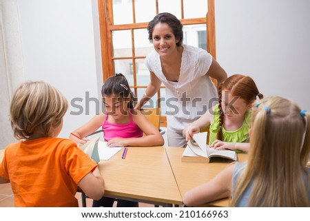 Pretty teacher standing with pupils at desk at the elementary school