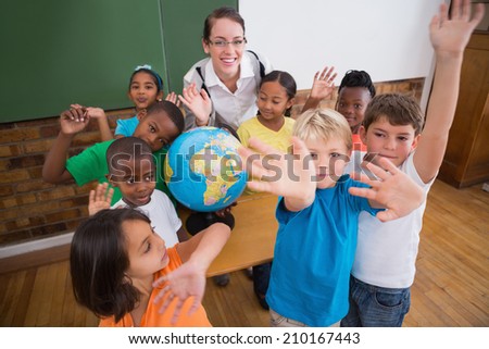 Cute pupils smiling around a globe in classroom with teacher at the elementary school