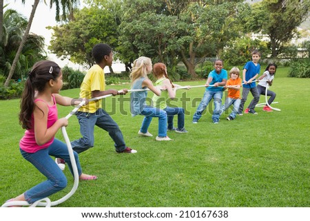 Cute pupils playing tug of war on the grass outside at the elementary school