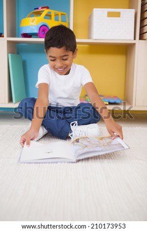 Cute little boy sitting on floor reading in classroom at the nursery school