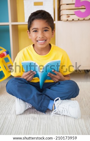 Cute little boy sitting on floor reading in classroom at the nursery school