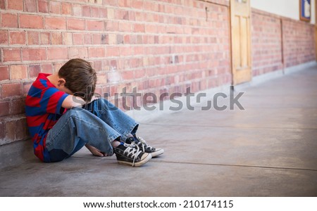 Sad pupil sitting alone in corridor at the elementary school