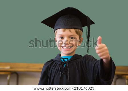 Cute pupil in graduation robe smiling at camera in classroom at the elementary school