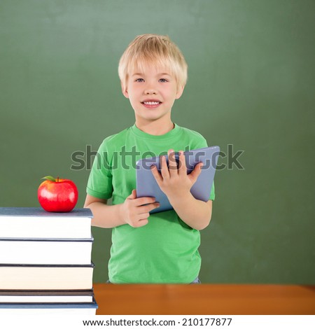 Cute boy using tablet against red apple on pile of books in classroom