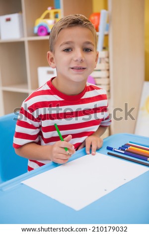 Cute little boy drawing at desk at the nursery school