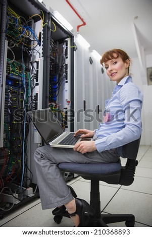 Happy technician sitting on swivel chair using laptop to diagnose servers in large data center