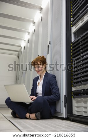 Technician sitting on floor beside server tower using laptop in large data center
