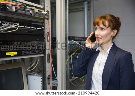 Pretty computer technician talking on phone beside open server in large data center