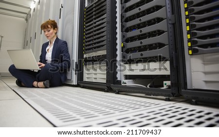 Technician sitting on floor beside server tower using laptop in large data center
