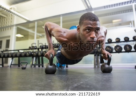 Determined shirtless muscular man doing push ups with kettle bells in the gym