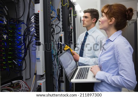 Team of technicians using digital cable analyser on servers in large data center