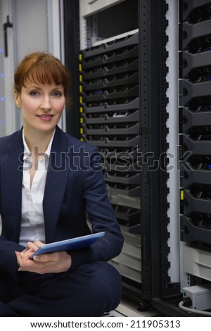 Happy technician sitting on floor beside server tower using tablet pc in large data center