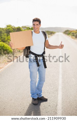 Portrait of a cheerful man hitchhiking with cardboard on countryside road