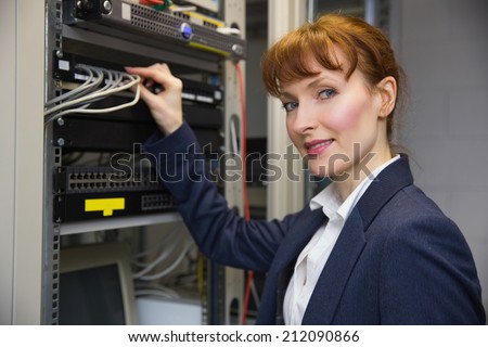 Pretty computer technician smiling at camePretty computer technician smiling at camera while fixing server in large data center