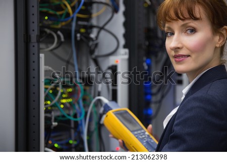 Happy technician using digital cable analyzer on server in large data center