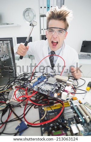 Angry computer engineer holding hammer over console in his office