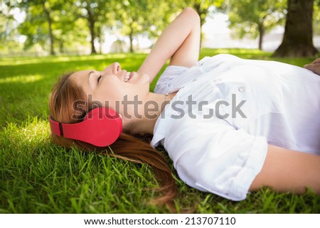Pretty redhead lying on grass listening to music on a sunny day