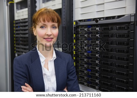 Pretty technician smiling at camera beside server tower in large data center