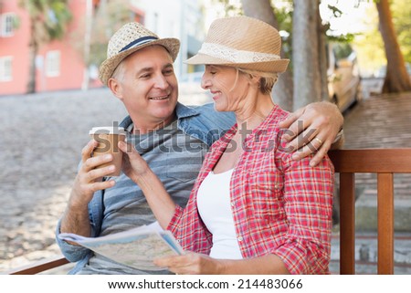 Happy tourist couple drinking coffee on a bench in the city on a sunny day